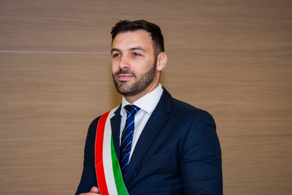 A confident man in a formal suit wearing an Italian flag sash, symbolizing professionalism and cultural pride.